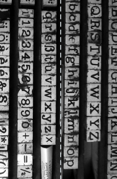 Schwarzweißaufnahme eines Stempelkastenalphabets, von einer senkrecht verlaufenden Linie aus weißen Gedankenstrichen und Leerzeichen geteilt, gleichsam auf dieser Linie geheftet.